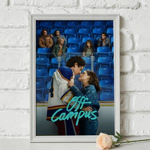 May include: Framed poster with a romantic scene from "Off Campus." A couple embraces in front of a hockey arena backdrop. The poster has a white frame and a light pink rose in the foreground. The title "Off Campus" is written in a teal script font.
