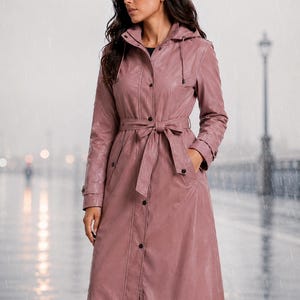 Puede incluir: Un impermeable largo de color rosa empolvado con capucha, cierre frontal de botones y un cinturón a juego para anudar en la cintura. El abrigo cuenta con mangas largas con puños ajustables, dos bolsillos laterales y un acabado liso e impermeable.