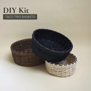 May include: Three woven baskets in different colors: brown, black, and white. The baskets are oval-shaped and have a textured appearance. The text "DIY Kit" and "TACO TRIO BASKETS" is visible in the image.