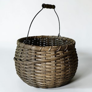 May include: A round, woven basket with a dark brown finish. The basket has a black metal handle with a wooden grip. The basket's woven design is visible throughout the body, and it has a sturdy, rustic appearance.