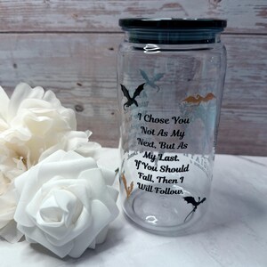 May include: A clear glass jar with a black lid, featuring dragon silhouettes and the text "I Chose You Not As My Next, But As My Last. If You Should Fall, Then I Will Follow." White roses are in the foreground.