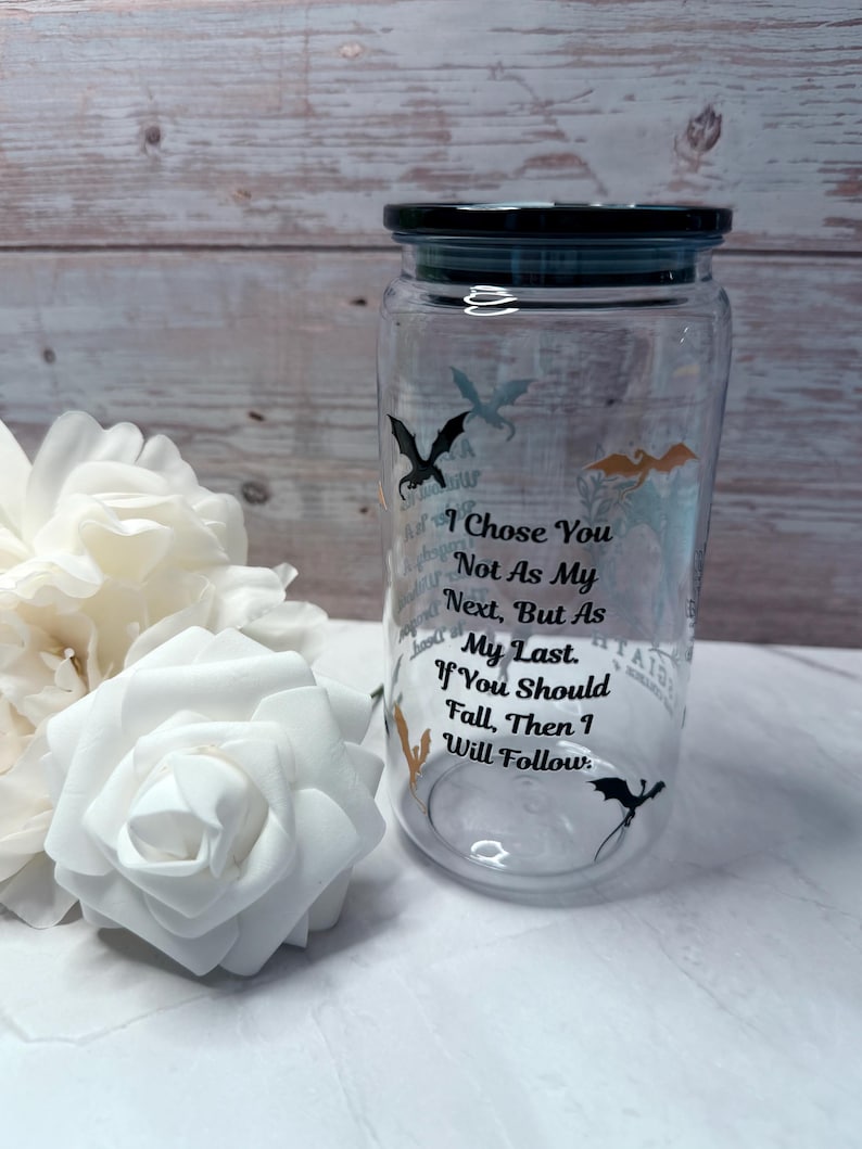 May include: A clear glass jar with a black lid, featuring dragon silhouettes and the text "I Chose You Not As My Next, But As My Last. If You Should Fall, Then I Will Follow." White roses are in the foreground.