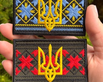 May include: Two rectangular embroidered patches featuring the Ukrainian Tryzub emblem in yellow. The top patch is black with blue geometric star patterns. The bottom patch is olive green with red geometric star patterns and black borders.