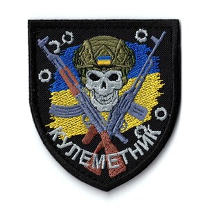 May include: Embroidered patch with a skull wearing a military helmet with a Ukrainian flag design. Two crossed rifles are behind the skull, with the Ukrainian flag colours in the background. The text "КУЛЕМЕТНИК" is below the skull.