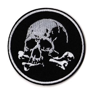 May include: Round black patch with a white embroidered skull and crossbones design. The skull has a distressed appearance, and the patch is bordered with a white stitched edge. A gothic or punk rock style.