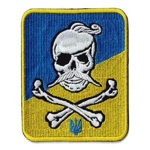 May include: A rectangular embroidered patch featuring a blue and yellow diagonal background. The design displays a white skull with a traditional Cossack hairstyle and mustache, positioned above crossed white bones and a small blue trident emblem.