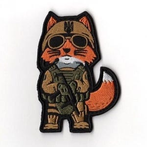 May include: Embroidered patch depicting a cartoon fox in military attire, wearing sunglasses and a helmet with a Ukrainian trident symbol. The fox is holding a rifle, with a black border and a white background.