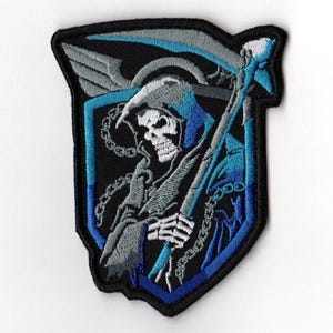 May include: Embroidered patch featuring a grim reaper in a blue hooded cloak, holding a scythe. The design is set against a black background within a shield shape, with blue and gray accents. The patch has a black border.