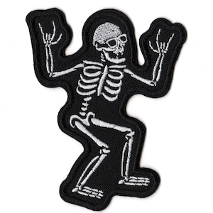 May include: An embroidered patch featuring a white skeleton on a black background. The skeleton is depicted in a squatting position with both arms raised and hands making a rock and roll hand gesture with extended index and pinky fingers.