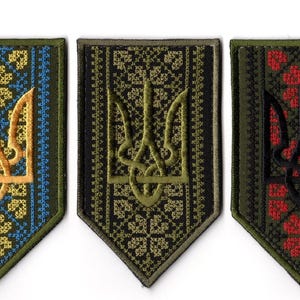 Könnte beinhalten: Drei gestickte Aufnäher mit dem ukrainischen Wappen, dem Tryzub. Jeder Aufnäher hat ein anderes Farbschema: Blau und Gold, Olivgrün und Schwarz mit roten Akzenten. Die Aufnäher sind schildförmig.