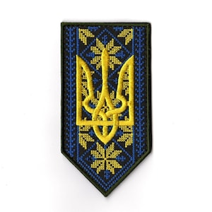 Puede incluir: Parche bordado con el escudo de armas ucraniano, un tridente dorado, sobre un fondo azul marino con detalles florales amarillos. El parche tiene un borde verde oscuro y una forma rectangular con la parte inferior puntiaguda.