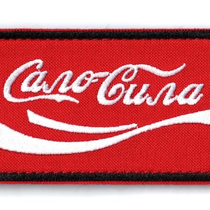 May include: Embroidered patch with a red background and the text "Caro-Cola" in white script. A white curved stripe is below the text. The patch has a black border.