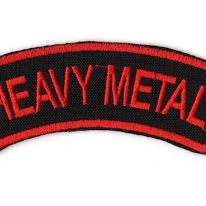 Puede incluir: Parche bordado con la frase "HEAVY METAL" en rojo sobre fondo negro. El parche tiene un borde rojo y una forma rectangular curvada. Ideal para chaquetas, bolsos u otras prendas.