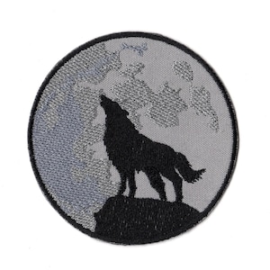 May include: A circular embroidered patch featuring a black silhouette of a wolf howling at a large, textured gray moon. The design is set against a light gray background with a dark gray border, creating a high-contrast graphic image.
