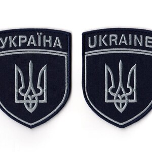 Op de afbeelding: Twee marineblauwe geborduurde patches. Elke patch heeft een schildvorm met het woord "UKRAINE" of "УКРАЇНА" in witte letters bovenaan. Daaronder is een zilveren drietandembleem gecentreerd. De patches hebben een zilveren rand.