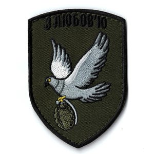 Puede incluir: Parche bordado con una paloma que lleva una granada. La paloma es blanca y gris, con pico y patas amarillas. El parche tiene el texto "З ЛЮБОВ'Ю" en verde sobre un fondo verde oscuro.