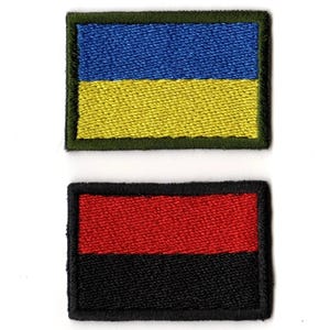 May include: Two embroidered patches. The top patch features a blue and yellow design, framed by a green border. The bottom patch displays a red and black design, framed by a black border. Both patches are rectangular.