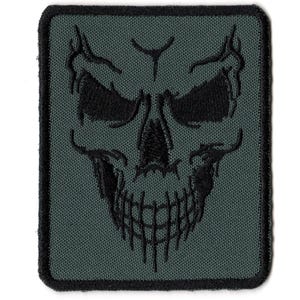 May include: A square, embroidered patch featuring a black skull design on a dark green background. The skull has detailed features, including eye sockets, a nose cavity, and a jagged jawline. The patch has a black border.
