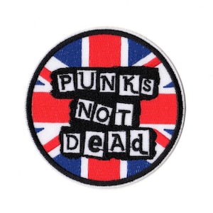 Puede incluir: Un parche bordado circular que presenta la bandera Union Jack en rojo, blanco y azul. Centrado en el parche hay un gráfico rectangular negro con texto blanco que dice PUNKS NOT DEAD en un estilo de fuente negrita, cuadrada y desgastada.