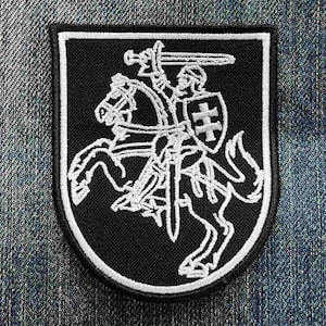 Puede incluir: Parche bordado en blanco y negro que representa a un caballero a caballo con una espada, un escudo y un casco. El parche tiene un fondo negro con un borde blanco y tiene forma de escudo. El diseño es un contorno detallado.