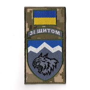 May include: A rectangular patch with a camouflage background. The patch features a blue and yellow flag at the top, with the text "ЗІ ЩИТОМ" in white. Below is a shield design with a wolf's head.