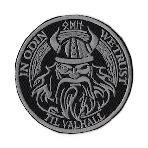 Puede incluir: Parche redondo bordado en negro y gris con un guerrero vikingo con casco con cuernos y barba. El texto "IN ODIN WE TRUST TIL VALHALL" está bordado alrededor de la imagen. El parche tiene un diseño detallado.