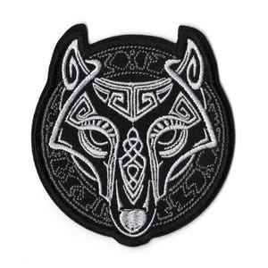 Può includere: Toppa ricamata nera con un disegno stilizzato di testa di lupo in bianco, ornata da intricati motivi a nodi celtici. La toppa ha una forma circolare con un bordo nero.