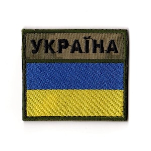 May include: A square patch featuring the Ukrainian flag design. The patch has a dark green border and a horizontal tricolor design of blue and yellow. The word "УКРАЇНА" is embroidered in dark green at the top.
