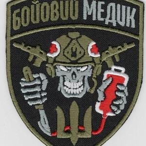 Puede incluir: Una taza de cerámica blanca con un asa negra y el texto "But First, Coffee" en negrita negra. La taza se encuentra sobre un fondo borroso, sugiriendo un ambiente acogedor.