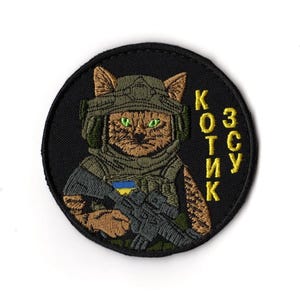 May include: Embroidered patch featuring a cat in military gear, holding a rifle. The cat has green eyes and wears a helmet and vest. The patch is round, with the text "KOTИK" in yellow.