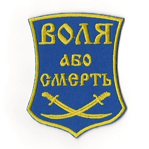 May include: Embroidered patch with a blue shield shape and gold trim. The patch features gold text that reads "VOLYA ABO SMERT" and two crossed gold swords.