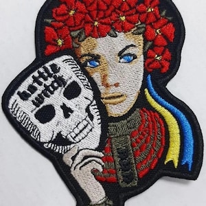 May include: Embroidered patch featuring a woman with blue eyes, a red floral crown, and a skull mask. The patch includes the text "bottle witch" and a blue and yellow ribbon. The design is set against a black background.