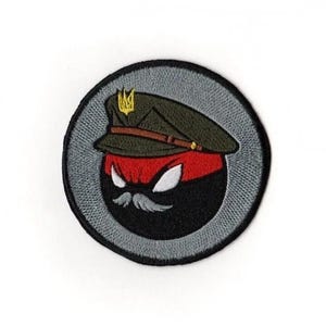 May include: Embroidered patch featuring a stylized character with a black and red face, a gray mustache, and a military-style cap. The cap is olive green with a gold emblem. The patch is circular with a gray border.