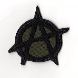 May include: Black embroidered patch featuring the anarchy symbol, a stylized letter "A" within a circle, with three outward-pointing spikes. The patch has a black border and a green fabric background.