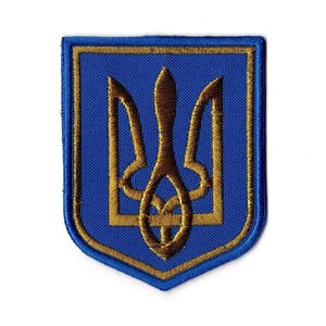 May include: Embroidered patch featuring the Ukrainian coat of arms, a gold trident, on a blue shield. The shield has a gold border and is set against a white background. The patch is likely for clothing or accessories.