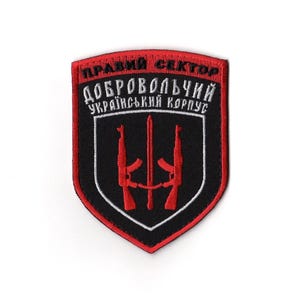 Puede incluir: Parche negro y rojo con el texto "ПРАВИЙ СЕКТОР" y "ДОБРОВОЛЬЧИЙ УКРАЇНСЬКИЙ КОРПУС" en letras blancas. El parche presenta dos rifles rojos y un diseño de espada.