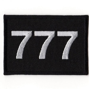 Puede incluir: Parche rectangular negro con el número "777" bordado en blanco. Los números están centrados en el parche, que tiene un borde negro. Adecuado para ropa o accesorios.