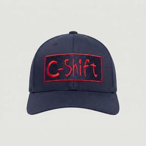 May include: Navy blue baseball cap with a curved brim. The cap features the embroidered text "C-Shift" in red within a red rectangular border. The cap has a button on top and a classic six-panel design.