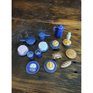 May include: Miniature blue and white speckled ceramic breakfast set. Includes a teapot, frying pans, plates with pancakes and eggs, cakes, and a pie. The set is arranged on a wooden surface.