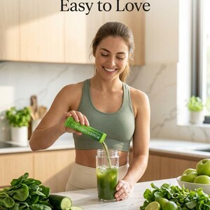 Puede incluir: Una mujer con un sujetador deportivo verde vierte un polvo verde de un paquete etiquetado como "POWER GREENS" en un vaso de agua con hielo. El texto "Simple to Mix / Easy to Love" est&aacute; en la parte superior. Productos frescos, espinacas, pepinos, limas y manzanas, est&aacute;n en el mostrador.