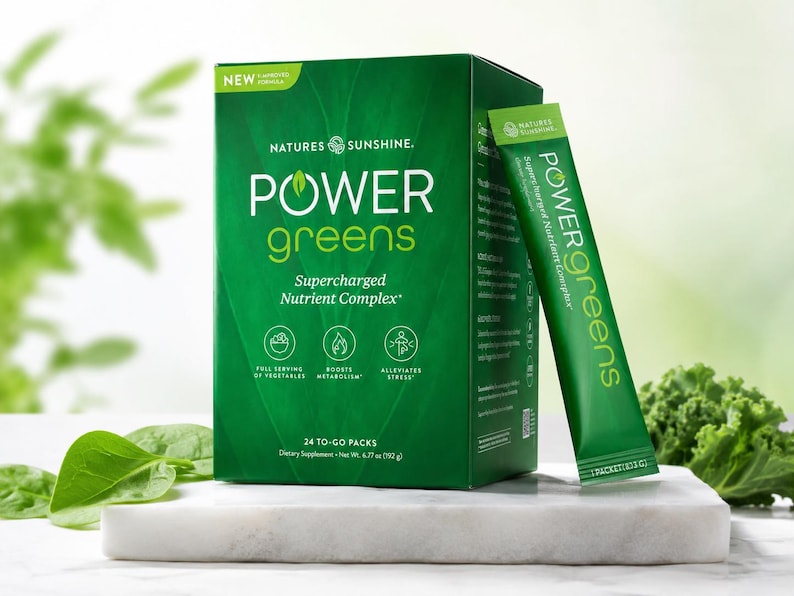 Puede incluir: Una caja verde de suplemento diet&eacute;tico "POWER greens" y un sobre. La caja tiene texto blanco que dice "Supercharged Nutrient Complex" y "24 to-go packs". El sobre dice "Supercharged Nutrient Complex". El producto se muestra sobre una superficie blanca.