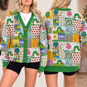 May include: A long-sleeve knit cardigan featuring a colorful patchwork pattern of The Very Hungry Caterpillar illustrations, including green caterpillars, suns, trees, and red hearts. The garment has a green V-neck collar and four brown buttons.