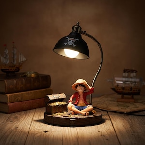 Könnte beinhalten: Schwarze Schreibtischlampe mit Piraten-Totenkopf-Design, mit einer Figur eines Charakters mit Strohhut und roter Jacke. Die Figur sitzt in der Nähe einer Schatzkiste voller Goldmünzen. Die Lampe steht auf einer Holzoberfläche.