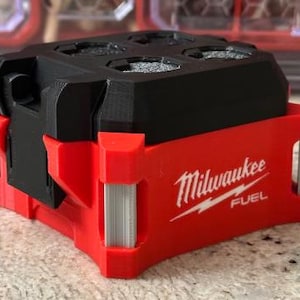 May include: A red and black Milwaukee FUEL tool accessory. The accessory has a red base with the Milwaukee logo and a black top with four circular openings. The accessory is designed to hold tools.