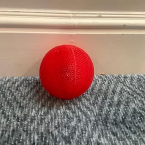May include: A bright red spherical ball featuring a fine, uniform mesh-like grid pattern across its entire surface. The object is round and displays a consistent, vibrant red color throughout its textured, perforated exterior construction.