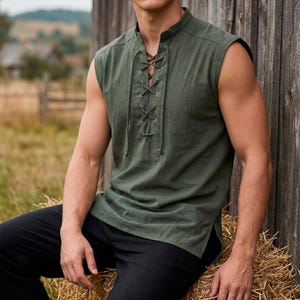 May include: Olive green sleeveless shirt with a lace-up front. The shirt has a mandarin collar and a relaxed fit. The model is wearing black pants. The shirt is made of a lightweight fabric, perfect for warm weather.