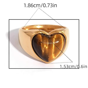 Peut inclure: Bague dorée avec une pierre en œil de tigre en forme de cœur. La bague mesure 1,86 cm de large et 1,53 cm de haut. Un bijou audacieux.