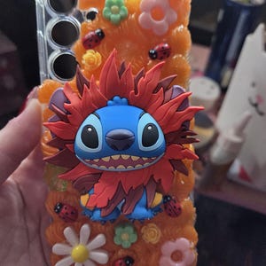 Può includere: Custodia trasparente per telefono decorata con finta pelliccia arancione, fiori, coccinelle e un personaggio Stitch blu con dettagli rossi. Design giocoso, ideale per i fan Disney.