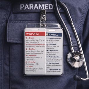 以下が含まれることがあります： 「PARAMED」と書かれたネームタグが付いた救急救命士の制服のクローズアップ。タグには、OPQRSTとSAMPLEという医療評価プロンプトが記載された2枚のカードが表示されています。聴診器が近くにぶら下がっています。