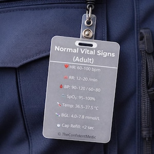 Puede incluir: Un uniforme de paramédico azul marino con un carrete de insignia que muestra un símbolo médico. Una etiqueta gris enumera los signos vitales normales en adultos, incluyendo la frecuencia cardíaca, la frecuencia respiratoria, la presión arterial, la SpO2, la temperatura y la glucosa en sangre.